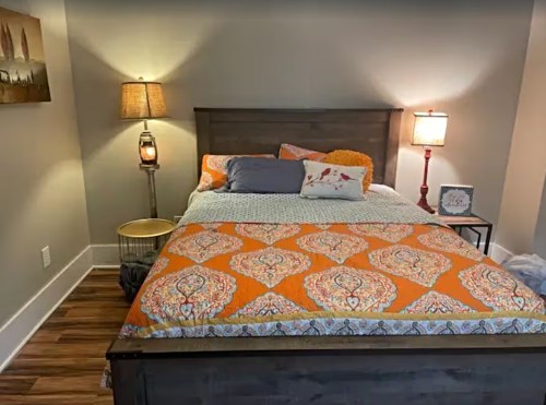 Cozy bedroom featuring a wooden bed with an orange patterned blanket, bedside lamps, and a decorative side table.