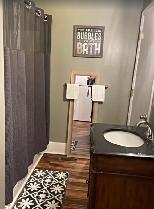 A bathroom with a shower curtain, mirror, sink, and decorative wall sign reading "You are the bubbles to my bath."