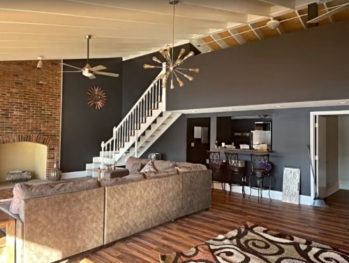 Modern living room with a large sectional sofa, staircase, and a kitchen area in a stylish, open layout.