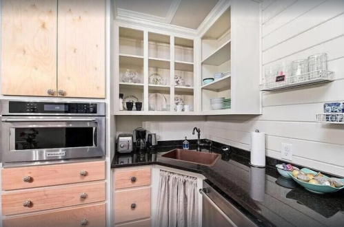 A modern kitchen with wooden cabinets, a black countertop, and open shelves displaying dishes and glassware.