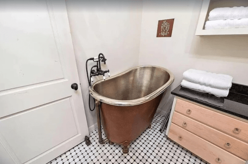 A vintage-style bathtub with a bronze finish, next to a black countertop and neatly stacked white towels.
