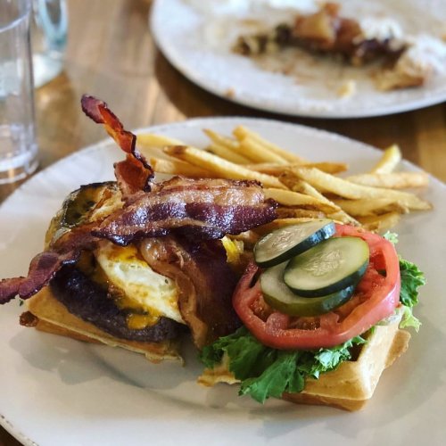 A hearty burger topped with bacon, lettuce, tomato, and pickles, served with a side of golden fries.