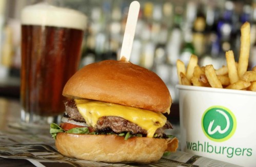 A juicy cheeseburger with lettuce and tomato, served with fries and a beer in the background.
