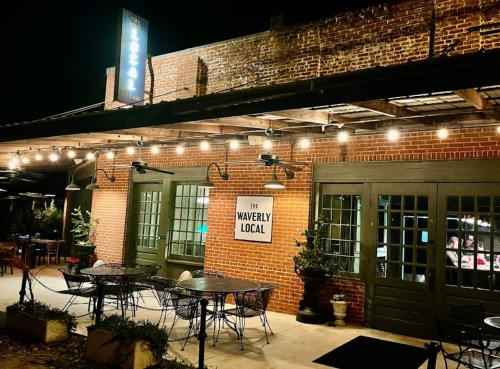 Exterior of The Waverly Local restaurant at night, featuring brick walls, string lights, and outdoor seating.