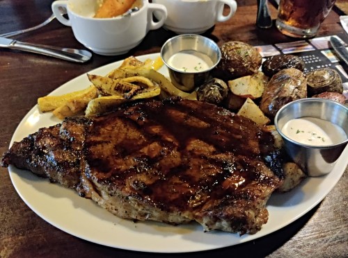 A plate featuring a grilled steak, roasted potatoes, and fried plantains, served with dipping sauces.