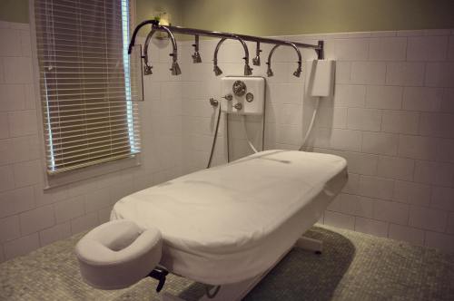 A clean, modern treatment room with a white massage table and multiple shower heads on the wall.