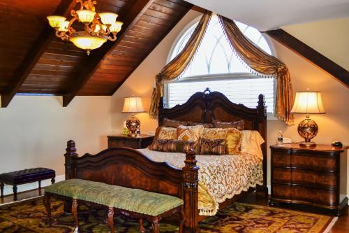 Cozy attic bedroom with a wooden bed, decorative bedding, two lamps, and a large window with elegant drapes.