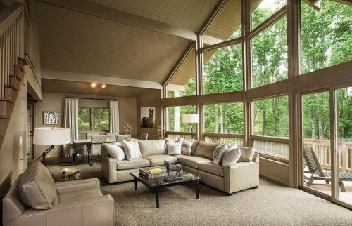 Spacious living room with large windows, modern furniture, and a view of greenery outside. Cozy and inviting atmosphere.