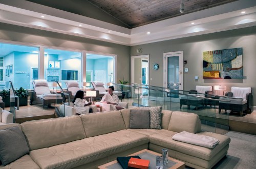 A modern spa lounge with a cozy sofa, relaxing guests in robes, and soft lighting creating a tranquil atmosphere.