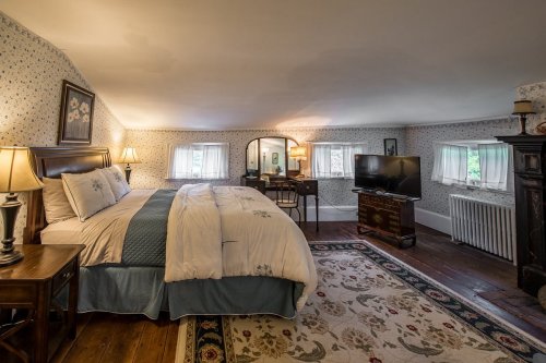 Cozy bedroom with a bed, TV, and vintage decor, featuring floral wallpaper and warm lighting.