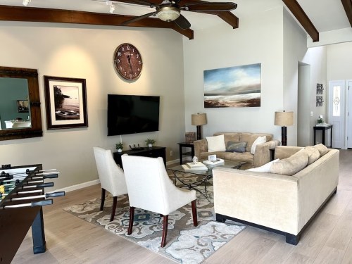 A cozy living room with a sofa, chairs, coffee table, TV, and decorative art on the walls. A foosball table is visible.