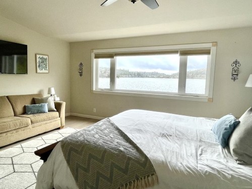 Cozy bedroom with a large window overlooking a lake, featuring a bed, sofa, and modern decor.