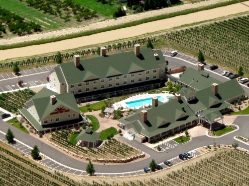 Aerial view of a hotel surrounded by vineyards, featuring a pool and landscaped grounds.