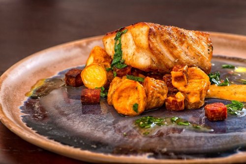 A beautifully plated dish featuring seared fish, roasted vegetables, and a drizzle of sauce on a rustic plate.