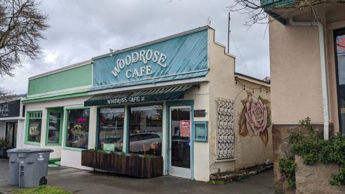 Exterior of Woodrose Cafe featuring a teal facade, open sign, and a large rose mural on the side.
