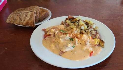 A plate of breakfast featuring scrambled eggs with sauce, potatoes, and toast on the side.