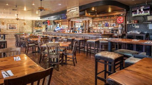 A cozy restaurant interior featuring wooden tables, chairs, a bar, and a TV displaying a sports game.