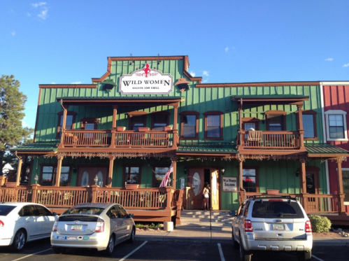 Exterior of a colorful restaurant named "Wild Women Saloon and Grill," featuring wooden balconies and a clear blue sky.