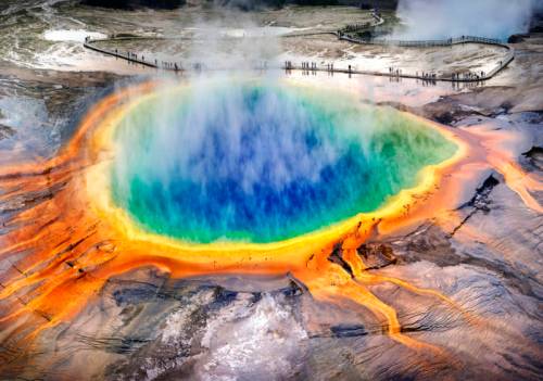 Aerial view of Yellowstone's Grand Prismatic Spring, showcasing vibrant blue, green, and orange colors with steam rising.