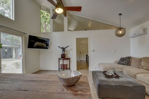 A modern living room with a ceiling fan, large windows, a TV, and a cozy sofa, featuring a decorative bowl on a table.