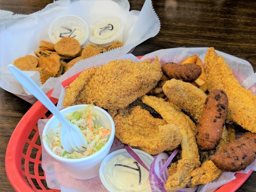 A basket of fried fish, hushpuppies, fries, and coleslaw, with a side of dipping sauces.