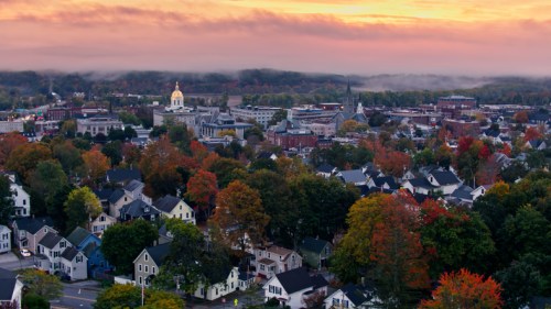 Aerial view of a town with colorful autumn trees, misty hills, and a golden dome building at sunset.