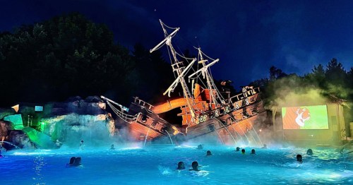 A shipwrecked pirate ship at night, surrounded by a glowing pool and mist, with a movie screen in the background.