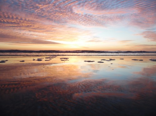 A serene beach at sunset, with colorful clouds reflecting on the water and gentle waves lapping at the shore.