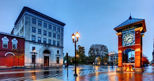 A rainy street scene featuring a historic building and a clock tower, with wet pavement reflecting the surroundings.