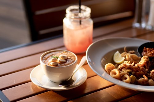 A bowl of soup with toppings, a plate of fried seafood, and a drink in a jar on a wooden table.