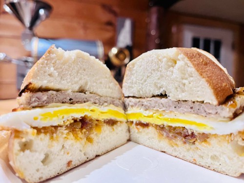 A close-up of a sandwich cut in half, featuring layers of egg, sausage, and cheese on a soft bun.