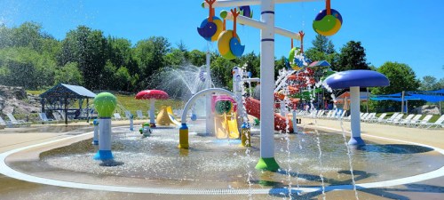 A colorful water play area with fountains, slides, and playful structures under a clear blue sky.