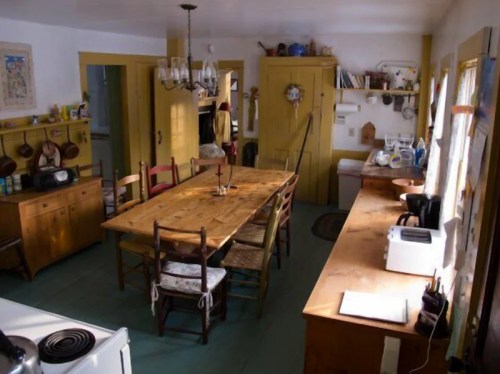 A cozy kitchen with a wooden dining table, chairs, and yellow walls, featuring rustic decor and appliances.