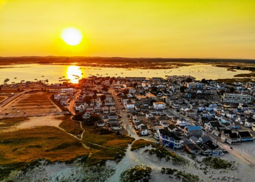 Aerial view of a coastal town at sunset, with boats in the water and a warm golden sky.