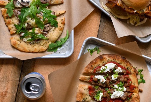 Three types of flatbreads and a burger on trays, with a can of soda in the foreground.