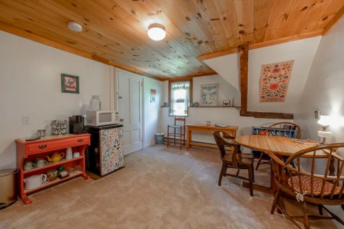 Cozy attic space with wooden ceiling, kitchenette, dining table, and decorative wall art. Warm and inviting atmosphere.