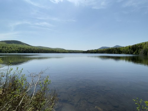 A serene lake surrounded by lush green hills under a clear blue sky, reflecting the landscape in calm waters.