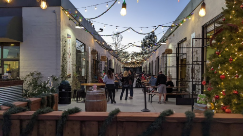 A festive outdoor space with string lights, people socializing, and holiday decorations in a lively atmosphere.