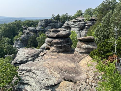 Rock formations surrounded by lush greenery and distant hills under a clear sky.