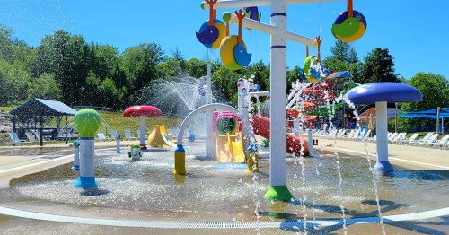 Colorful water play area with slides, fountains, and spray features under a clear blue sky.