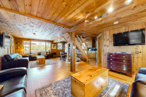 Cozy wooden living room with leather sofas, a coffee table, and large windows, featuring warm lighting and rustic decor.