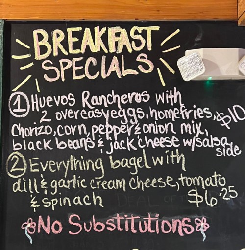 Chalkboard menu listing breakfast specials: huevos rancheros and an everything bagel with cream cheese and spinach.