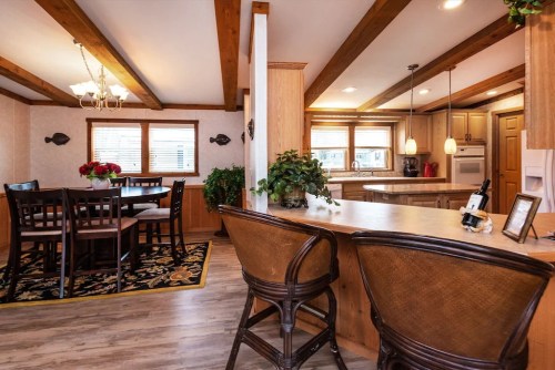 Cozy kitchen and dining area with wooden beams, a large table, and bar seating, featuring plants and warm lighting.