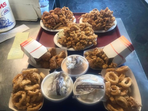 A tray filled with various fried chicken dishes, onion rings, and sides, arranged in multiple containers.