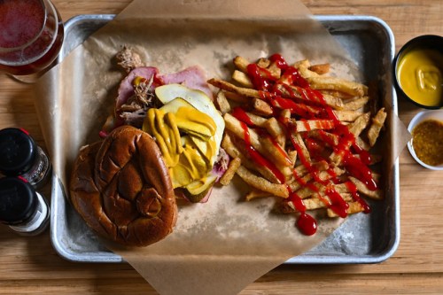 A tray with a pulled pork sandwich, pickles, mustard, and a side of fries drizzled with ketchup.