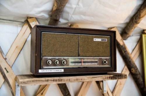 A vintage wooden radio with two speakers, displayed on a wooden shelf against a textured background.