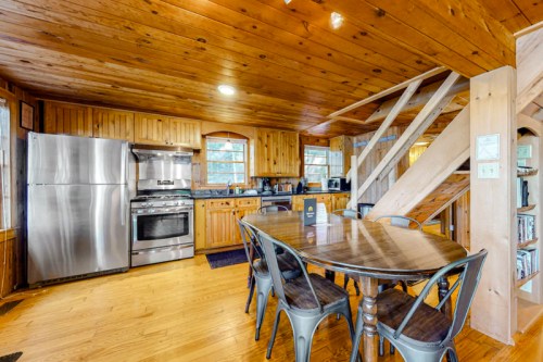 Cozy wooden kitchen with stainless steel appliances and a round dining table, featuring a staircase in the background.