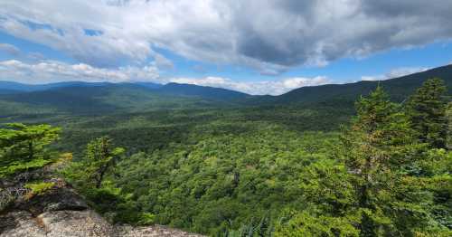 A panoramic view of lush green mountains and valleys under a partly cloudy sky.