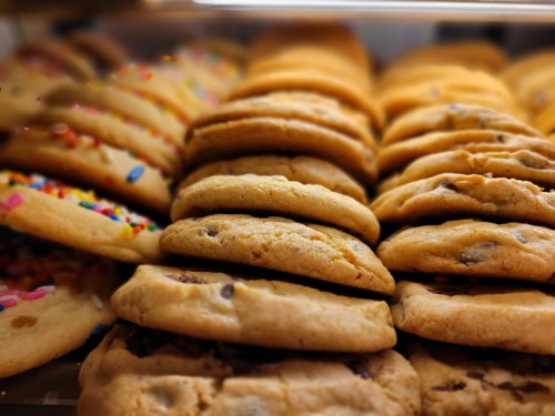 A close-up of a variety of cookies stacked together, including chocolate chip and sprinkle-topped cookies.