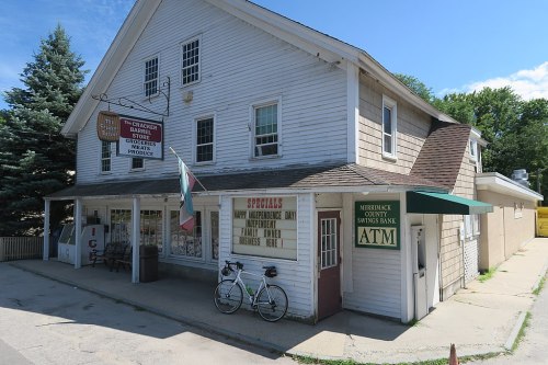 A quaint white building with a green awning, featuring a bank ATM and a bicycle parked outside.